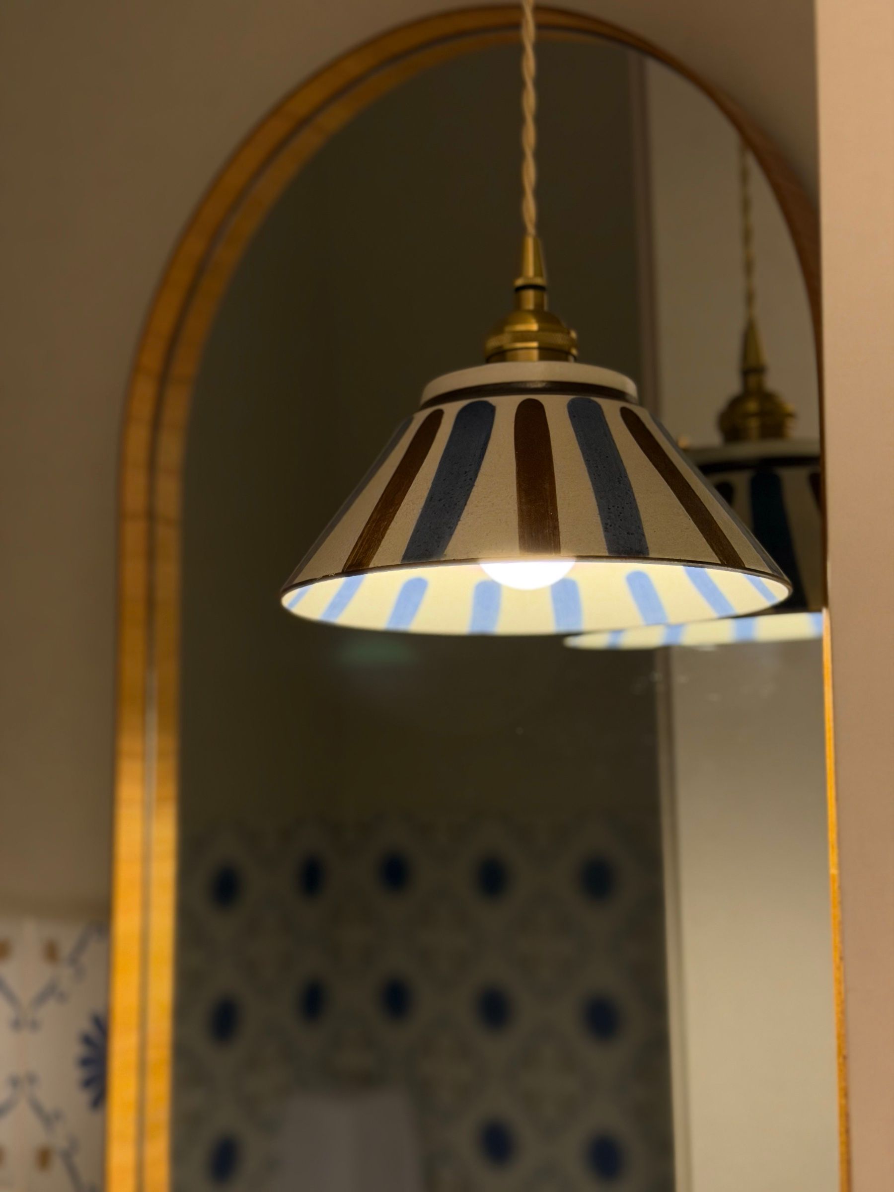 Luminária acesa diante de um espelho em arco na Clínica Benvenuta